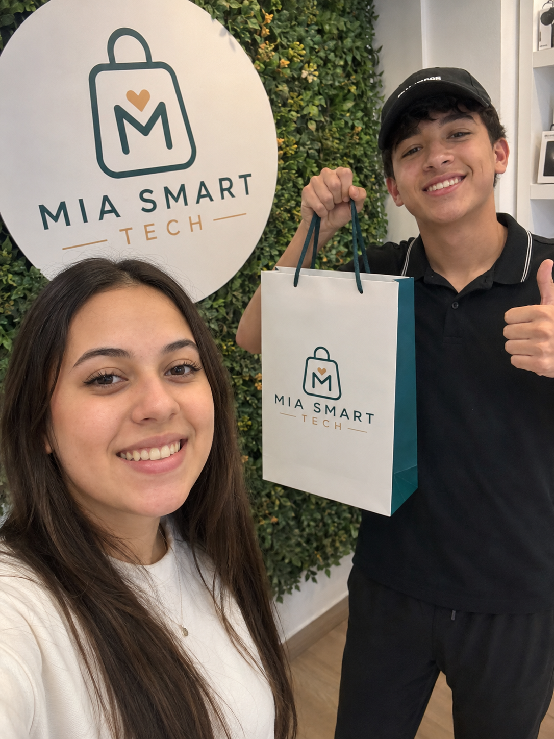 Dos clientes sonrientes mostrando su bolsa de compra frente al logo de MIA SMART TECH